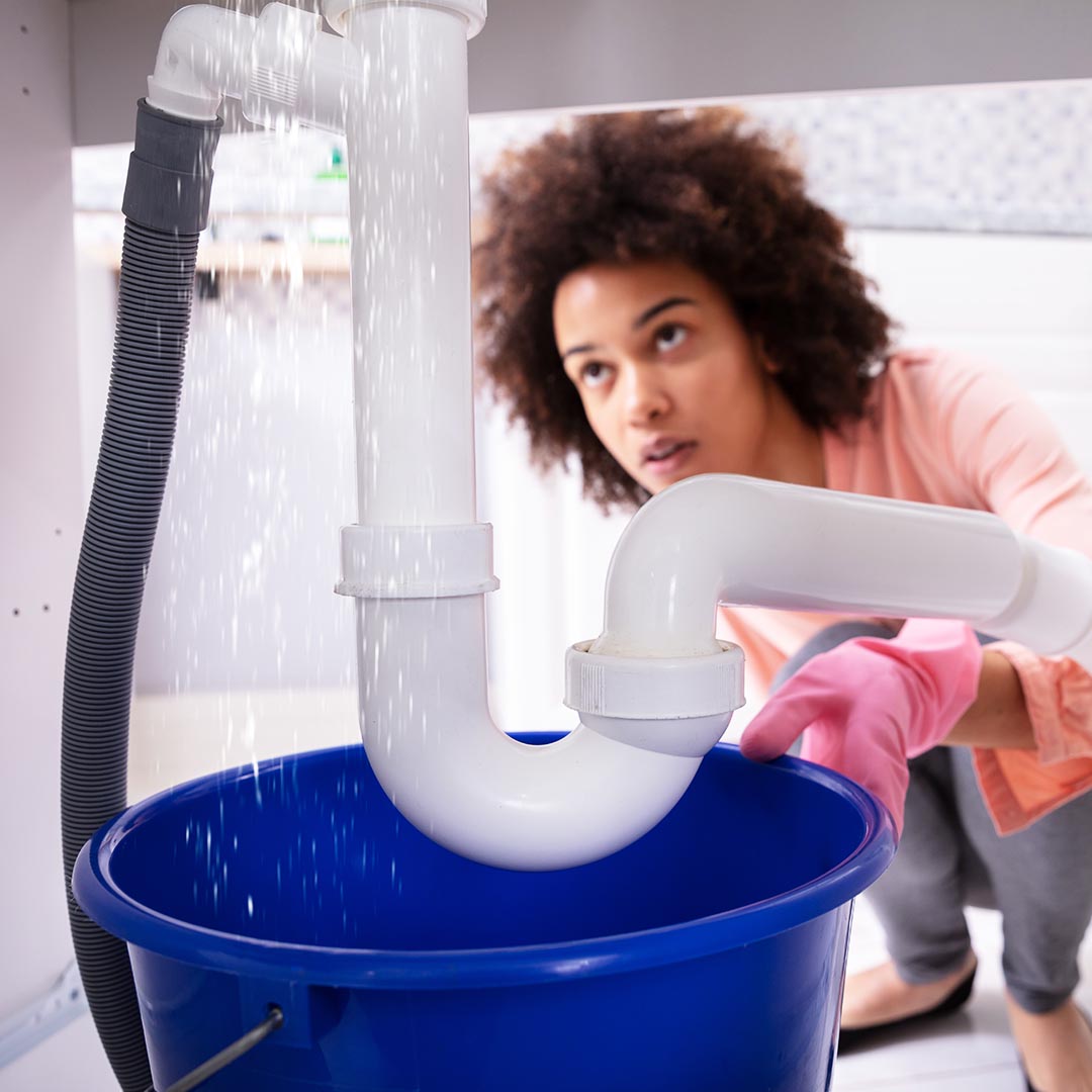 woman putting a bucket under leaking pipes under sink