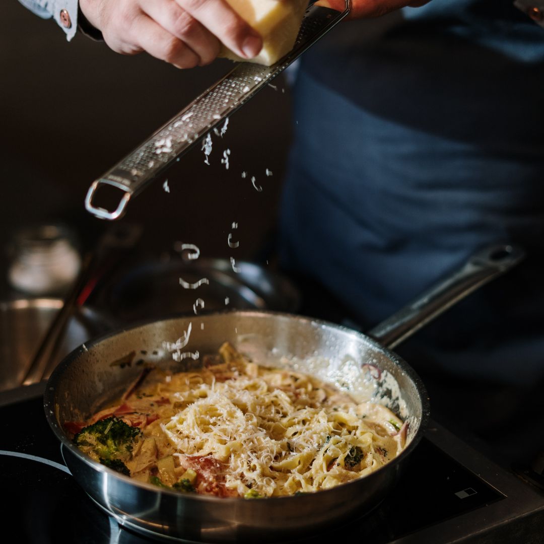 A chef shredding parmasean over a dish of pasta