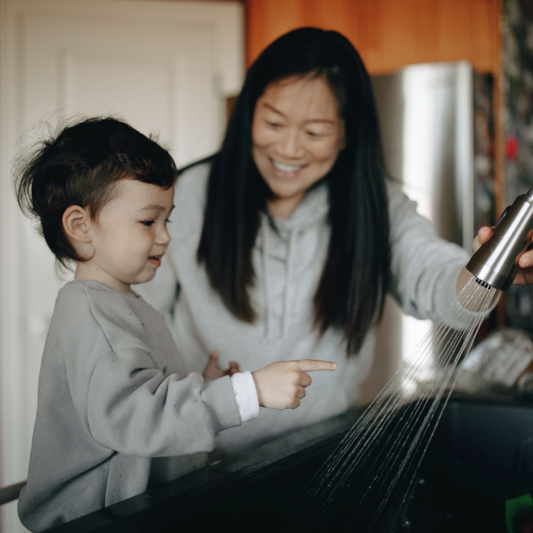 A mom and her young son washing their hands in a kitchen sink